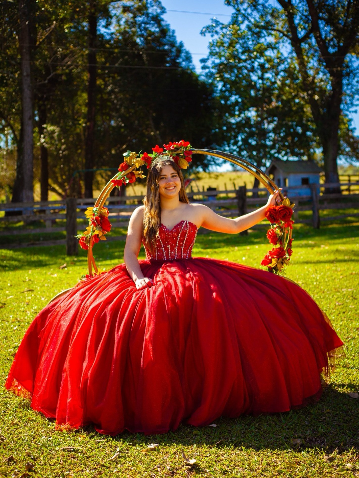Debutante de vestido vermelho em meio a arco de flores no campo